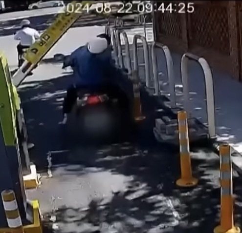 73歲婦人騎機車22日上午9點44分，要離開台中榮民總醫院嘉義分院停車場，疑似硬闖，結果臉撞柵欄，手又催油門失控，當場摔在路中央受傷，全程被監視器拍下。記者魯永明／翻攝