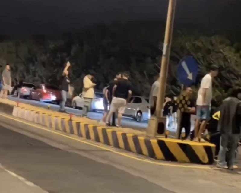 桃園市大園區昨深夜出現大批改裝車輛聚集，數10名黑衣人聚集在國際路3段，站在路邊及中央分隔島占用道路。記者周嘉茹／翻攝