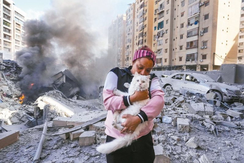 以軍二日空襲黎巴嫩貝魯特，一名女子抱著貓站在一棟被毀建築前。（美聯社）
